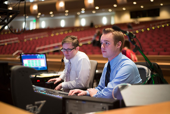 Josh Foster (in blue shirt) and student assistant control the Audio Visual Console on ground floor of the I-Center.