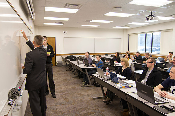 Brother Kevin Packard teaches helps a student solve a problem on the whiteboard in the Intermediate Financial Accouting class in the Smith Building.