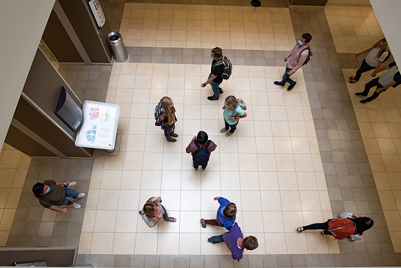 Examples of students staying safe and healthy during the COVID-19 pandemic by social distancing, following pathway arrows, and wearing face masks.