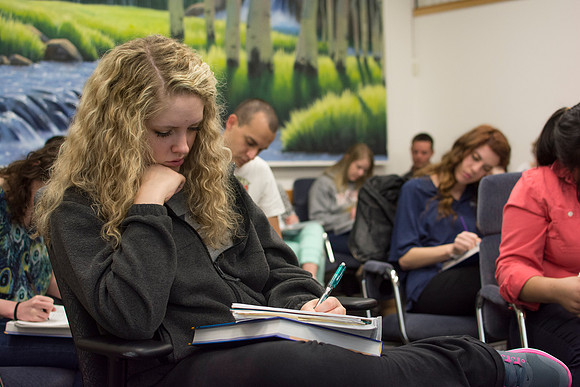 A student takes notes as she listens to Brother Clay talk about the self-serving bias.